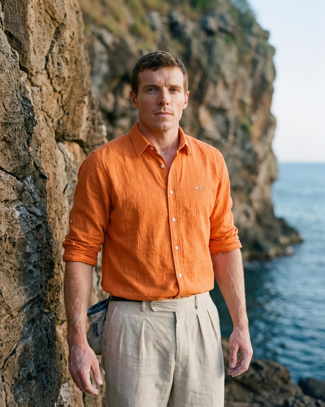 A climber in an orange linen shirt at the top of a sea cliff